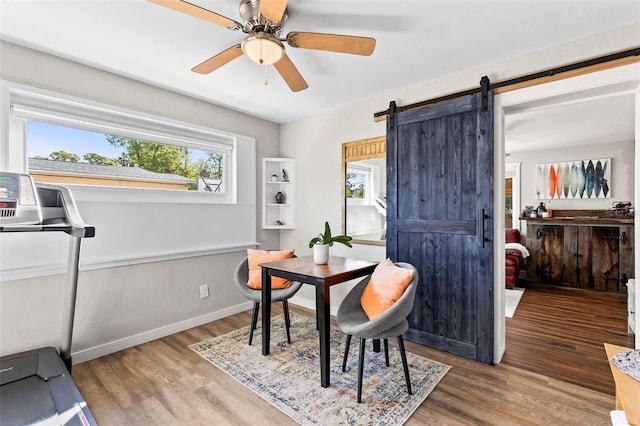 dining space featuring a barn door, baseboards, wood finished floors, and a ceiling fan