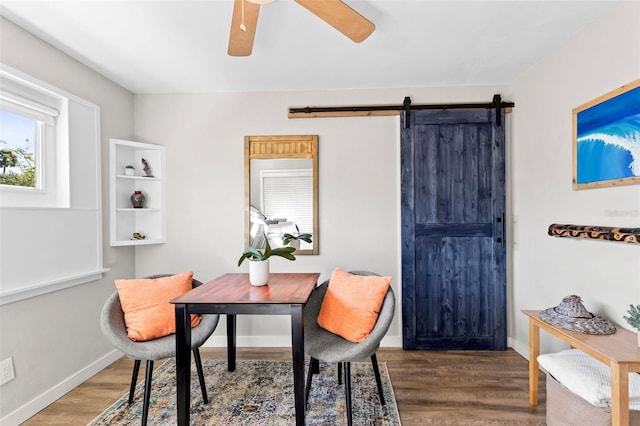 dining area featuring a barn door, wood finished floors, baseboards, and ceiling fan