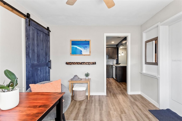 interior space featuring light wood finished floors, ceiling fan, baseboards, and a barn door