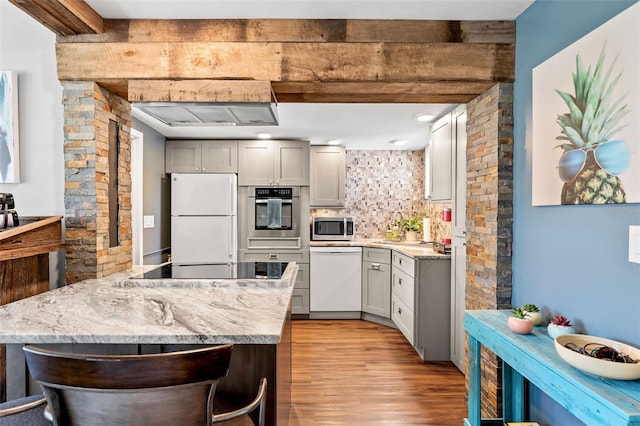 kitchen with tasteful backsplash, a peninsula, wood finished floors, white appliances, and a sink