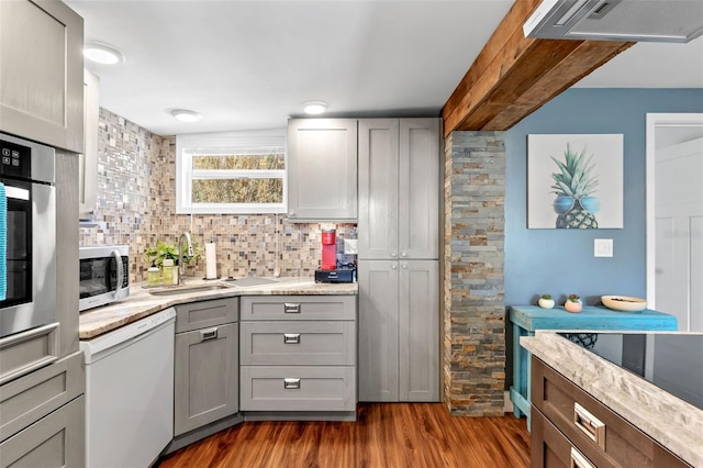 kitchen with backsplash, gray cabinetry, dark wood-type flooring, stainless steel appliances, and a sink