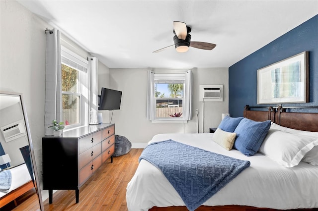 bedroom featuring multiple windows, baseboards, a wall mounted AC, and light wood-style floors