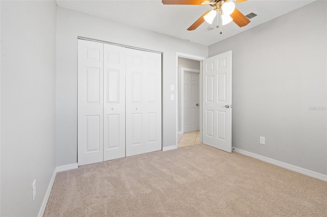 unfurnished bedroom with visible vents, a textured ceiling, a closet, baseboards, and light colored carpet