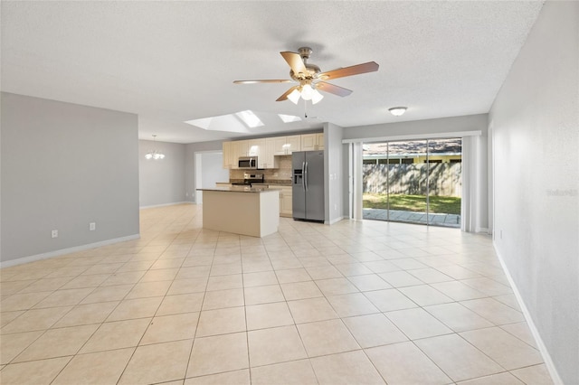 interior space featuring ceiling fan with notable chandelier, a textured ceiling, open floor plan, appliances with stainless steel finishes, and a skylight