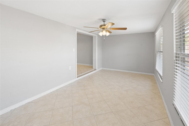 empty room with light tile patterned floors, a ceiling fan, and baseboards