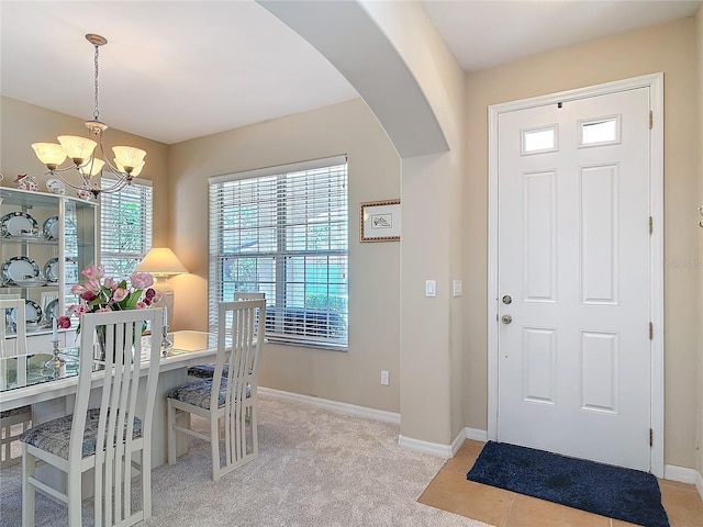 entryway featuring an inviting chandelier, baseboards, arched walkways, and light carpet