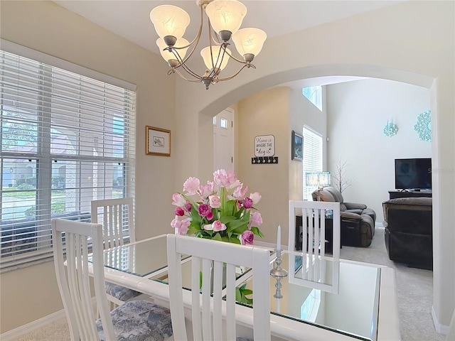 carpeted dining room with arched walkways, baseboards, and an inviting chandelier