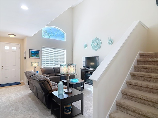 living area with stairs, light colored carpet, baseboards, and a towering ceiling