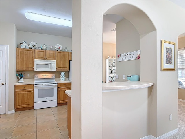 kitchen featuring white appliances, light tile patterned flooring, arched walkways, light countertops, and brown cabinets