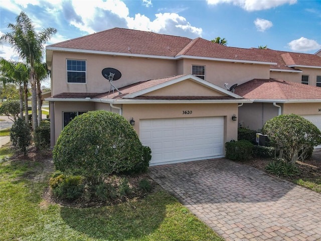 traditional home with decorative driveway, a shingled roof, an attached garage, and stucco siding