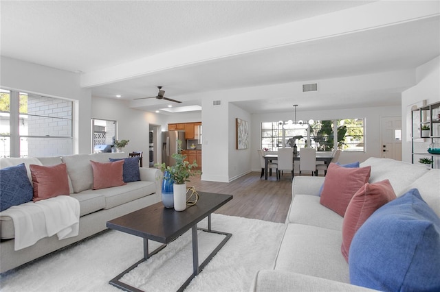 living room featuring light wood-type flooring, visible vents, baseboards, and ceiling fan with notable chandelier