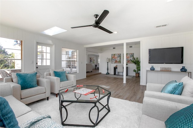 living room with a skylight, wood finished floors, visible vents, and ceiling fan