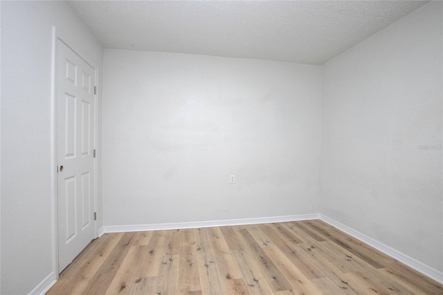 spare room with baseboards, a textured ceiling, and light wood finished floors