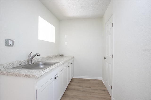 kitchen featuring a sink, light countertops, light wood-style floors, a textured ceiling, and white cabinetry