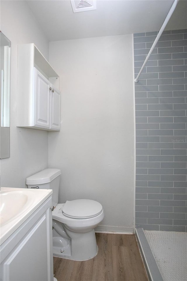 bathroom with visible vents, tiled shower, toilet, and wood finished floors