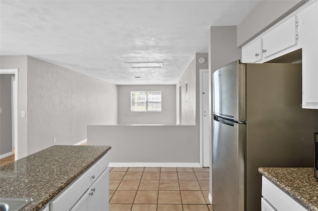 kitchen with baseboards, dark stone counters, freestanding refrigerator, light tile patterned flooring, and white cabinetry