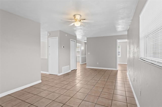 empty room featuring light tile patterned floors, visible vents, baseboards, and ceiling fan