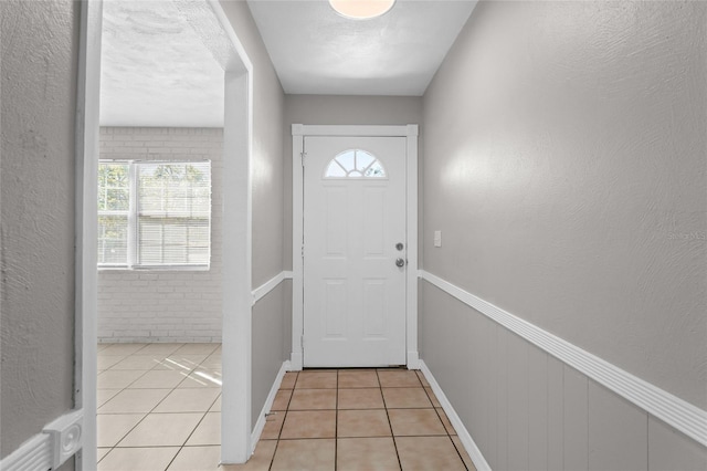 doorway to outside with light tile patterned floors, a healthy amount of sunlight, a textured wall, and wainscoting