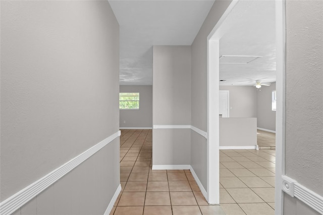 hallway featuring attic access, light tile patterned flooring, and baseboards