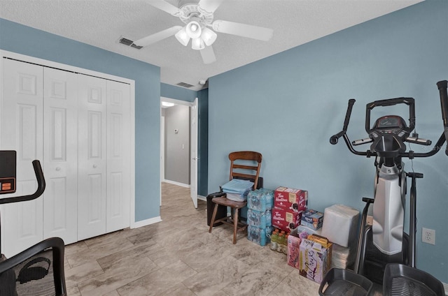 exercise area with baseboards, a ceiling fan, visible vents, and a textured ceiling