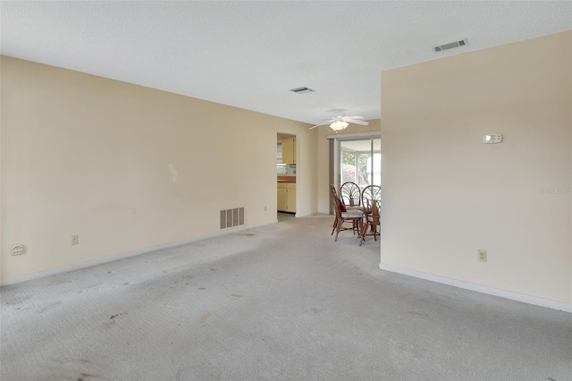 empty room featuring light carpet, visible vents, a textured ceiling, and a ceiling fan