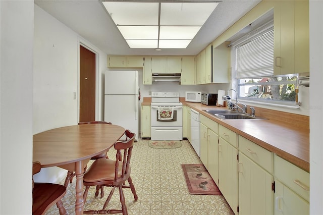 kitchen featuring cream cabinetry, under cabinet range hood, a sink, white appliances, and light floors