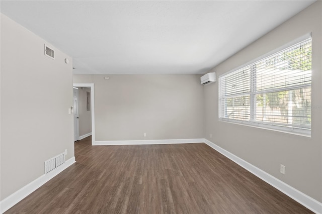 spare room featuring a wall unit AC, baseboards, visible vents, and dark wood-style flooring