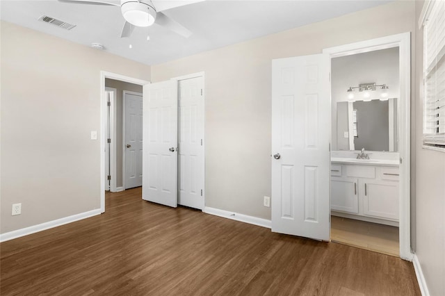 unfurnished bedroom with baseboards, visible vents, a sink, dark wood-type flooring, and ensuite bathroom