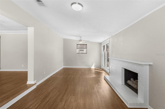 unfurnished living room with visible vents, a textured ceiling, wood finished floors, baseboards, and a brick fireplace