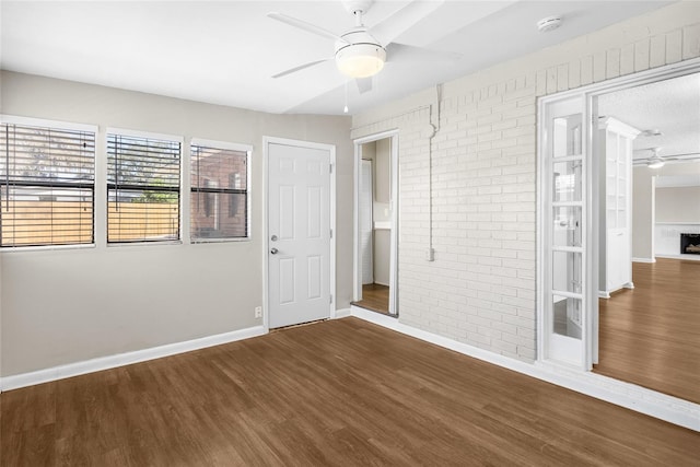 unfurnished bedroom featuring baseboards, wood finished floors, and brick wall