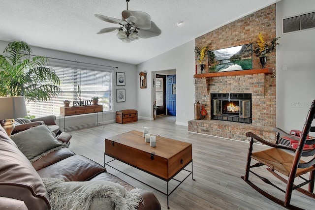 living room with wood finished floors, visible vents, ceiling fan, a textured ceiling, and a brick fireplace