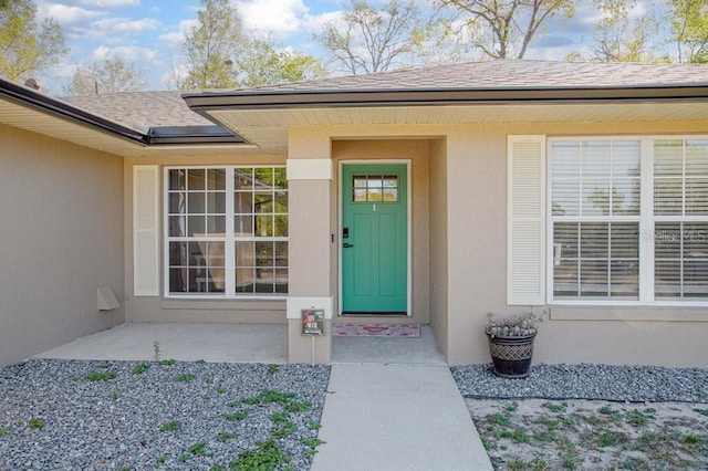 entrance to property with stucco siding and roof with shingles