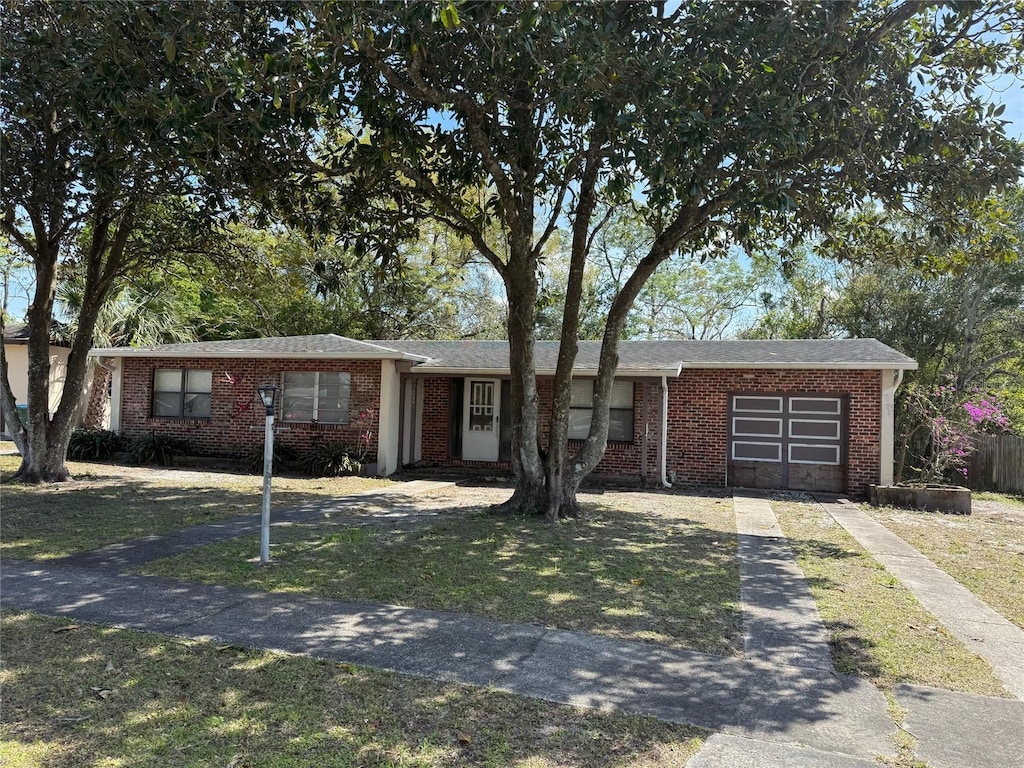 single story home featuring brick siding, a front lawn, an attached garage, and driveway