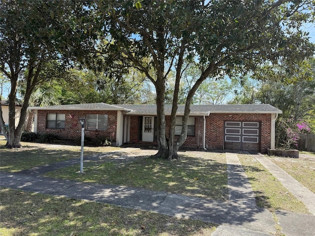 single story home featuring brick siding, a front lawn, an attached garage, and driveway