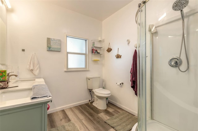 bathroom featuring toilet, baseboards, a stall shower, double vanity, and wood finished floors