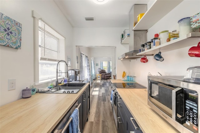 kitchen with open shelves, stainless steel microwave, wooden counters, a sink, and wood finished floors