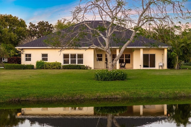back of house featuring a water view, stucco siding, and a yard