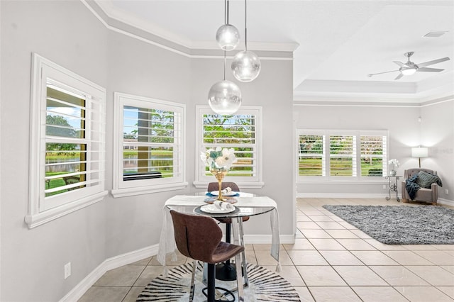 dining space with light tile patterned flooring, ceiling fan, baseboards, a tray ceiling, and ornamental molding