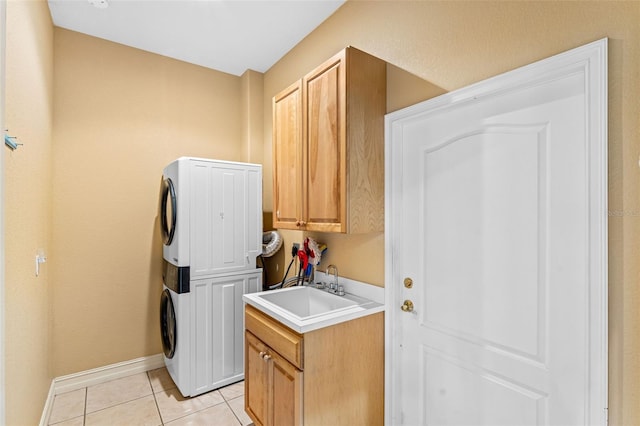 clothes washing area with cabinet space, a sink, light tile patterned floors, baseboards, and stacked washer and clothes dryer