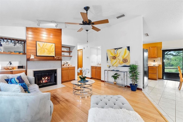 living area featuring light wood-style flooring, a large fireplace, ceiling fan, and vaulted ceiling