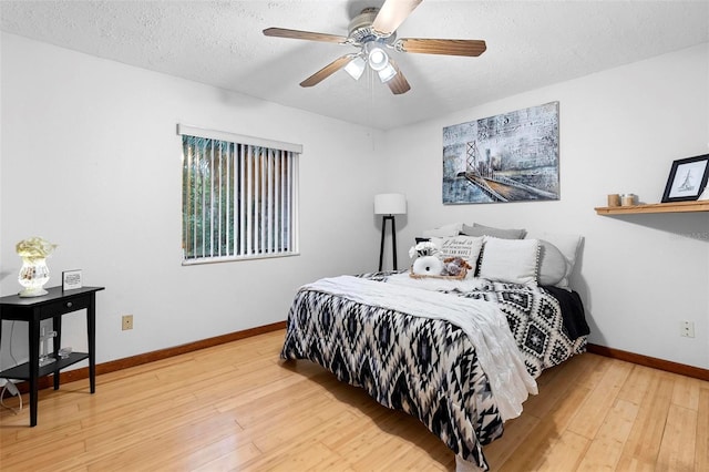 bedroom featuring ceiling fan, a textured ceiling, light wood-type flooring, and baseboards