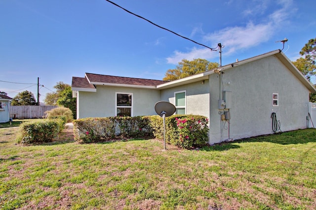 view of side of home with stucco siding, a yard, and fence
