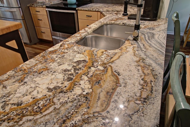 kitchen with light brown cabinets, light stone countertops, appliances with stainless steel finishes, wood finished floors, and a sink