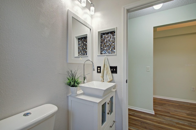 bathroom with baseboards, toilet, vanity, wood finished floors, and a textured ceiling