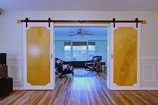 hall with a barn door, wood finished floors, and a textured ceiling
