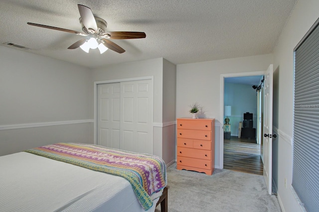 bedroom featuring a ceiling fan, visible vents, a closet, a textured ceiling, and carpet flooring