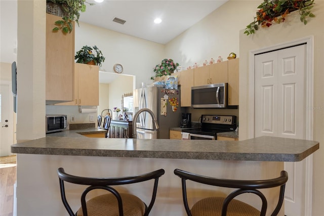 723 Pelican Ct, Kissimmee, FL 34759 - kitchen with dark countertops, a kitchen breakfast bar, light brown cabinets, and appliances with stainless steel finishes