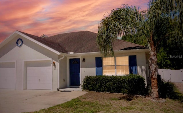 view of front of property featuring fence, a shingled roof, an attached garage, stucco siding, and driveway