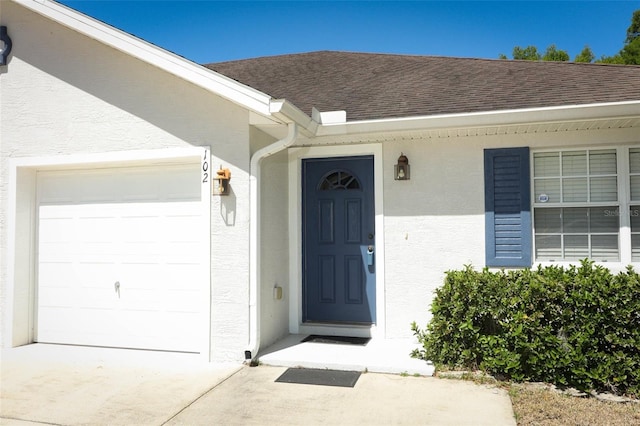 entrance to property with a garage, roof with shingles, stucco siding, and concrete driveway