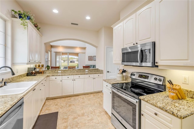 3145 Connemara Dr, Ormond Beach, FL 32174 - kitchen with appliances with stainless steel finishes, a sink, arched walkways, light stone countertops, and white cabinetry